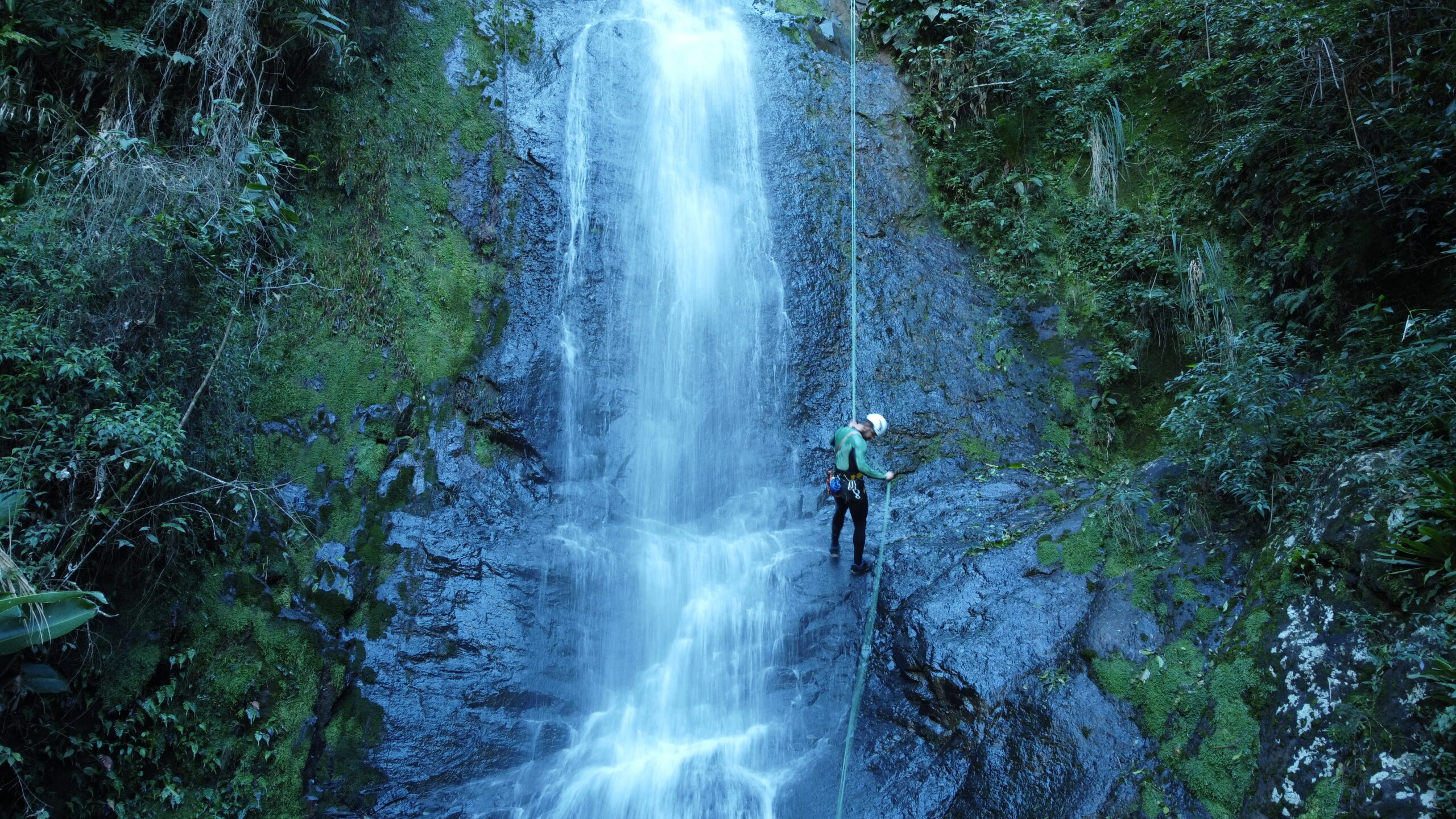 Pessoa descendo em um rapel na frente de uma cachoeira